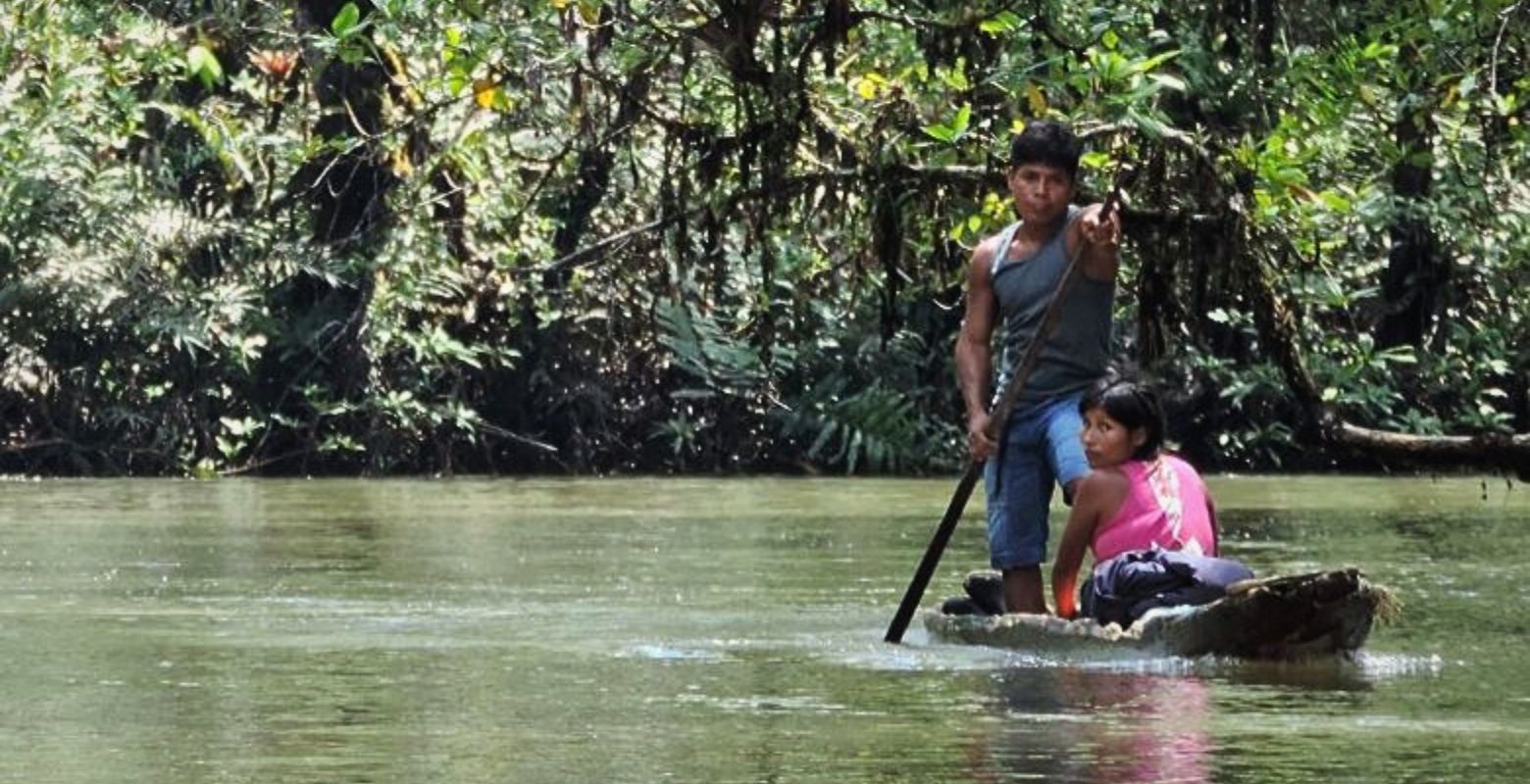 Integrantes de la comunidad Emberá-Wounaan navegan en una canoa tradicional por un río de Bahía Málaga, rodeados de selva tropical.